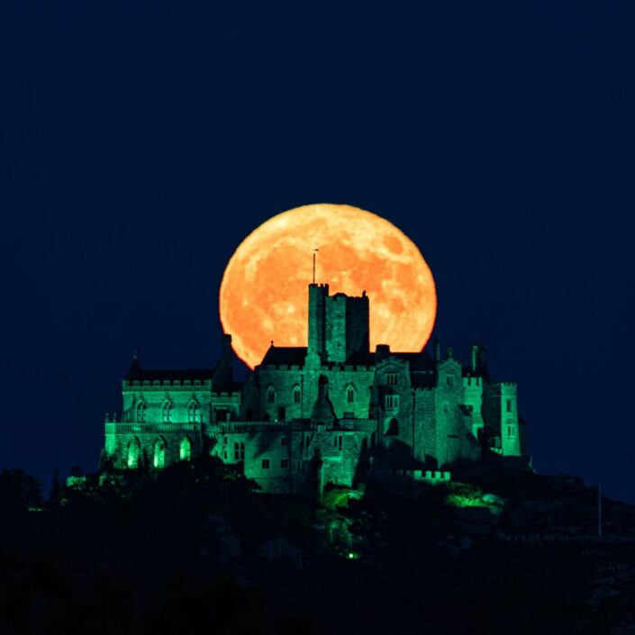St. Micahel's Mount, lit up in green, with a yellow supermoon rising behind it.